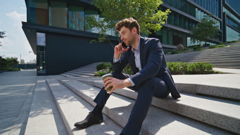 relaxed ceo talking mobile phone sitting urban stairs with coffee cup zoom in.