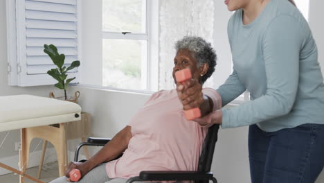 caucasian nurse with senior woman in wheelchair exercising with copy space, slow motion