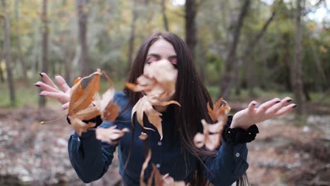 Slow-motion-shot-of-a-beautiful-gothic-woman-in-vintage-clothing-blowing-leaves-at-the-camera