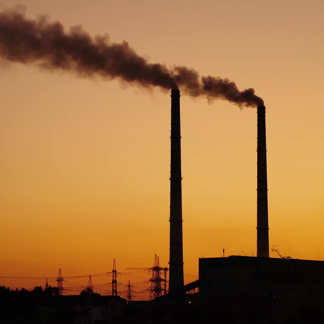 Dark pipes with emissions on the orange sky background. Dirty smoke coming from industrial pipes into the air at sunset. Pollution the environment.