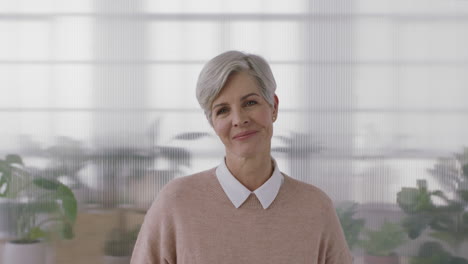 portrait of sophisticated mature business woman smiling looking at camera enjoying successful lifestyle senior female wearing jersey in office workspace background