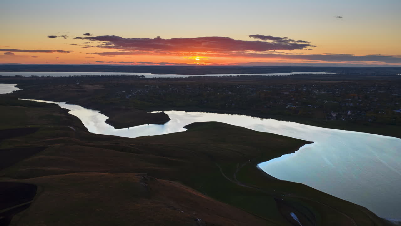 Aerial drone view of a winding river reflecting the warm sunset light over Moldova's rolling hills and distant villages time lapse