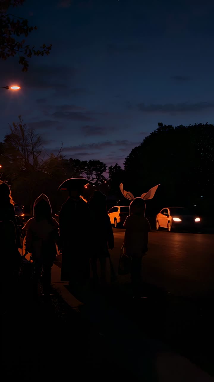 Vertical video: Dusk falling, parent guiding kids trick-or-treating on suburban street with buckets