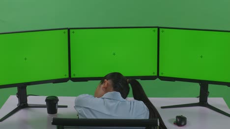 녹색 스크린 스튜디오에서 모의 여러 컴퓨터 모니터와 함께 일하면서 잠을 자는 피곤한 아시아 여성의 뒷면