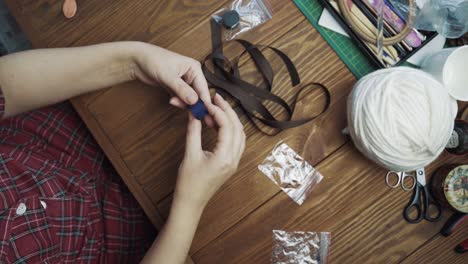 woman in pyjamas sitting and twist brown ribbon into roll.