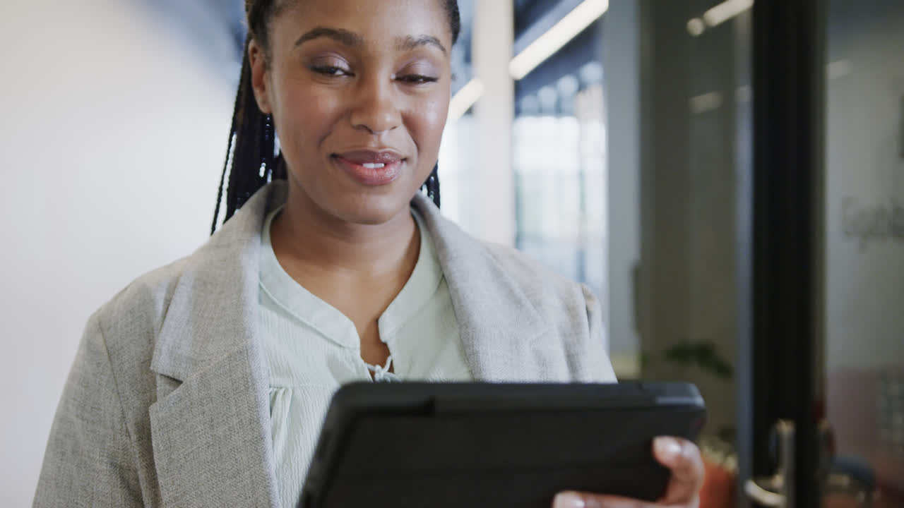 Ritratto di una felice donna d'affari afroamericana in abbigliamento casual che usa un tablet nel corridoio dell'ufficio, slow motion