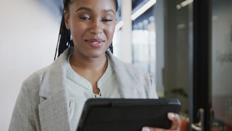 portrait of happy african american casual businesswoman using tablet in office corridor, slow motion