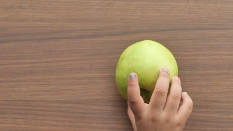 child's hand touching a green mango on a wooden table