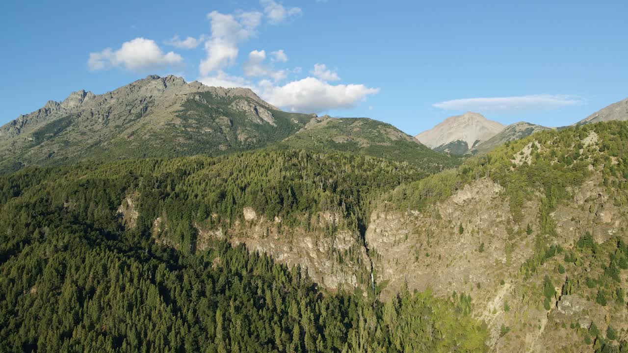 dolly aéreo que se eleva sobre montañas cubiertas de bosques de pinos y cascada de corbata blanca en el fondo, patagonia argentina