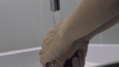 unrecognizable married person rinsing hands under bathroom water tap. slow motion