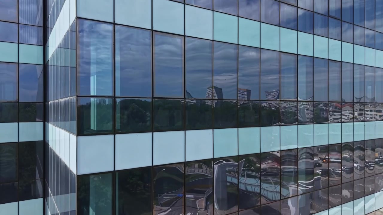 Vista di un edificio moderno con finestre di vetro che riflettono il cielo e gli alberi nell'area circostante di giorno.