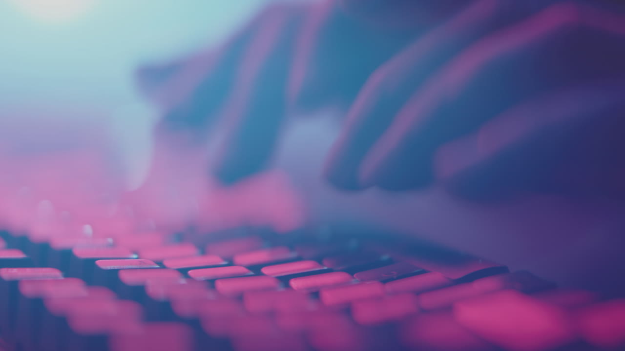 manos escribiendo en un teclado a la luz de neón