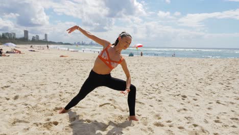 chica deportiva haciendo yoga en la playa - ángulo lateral extendido para invertir la pose del guerrero - guerrero ii - costa dorada, qld, australia