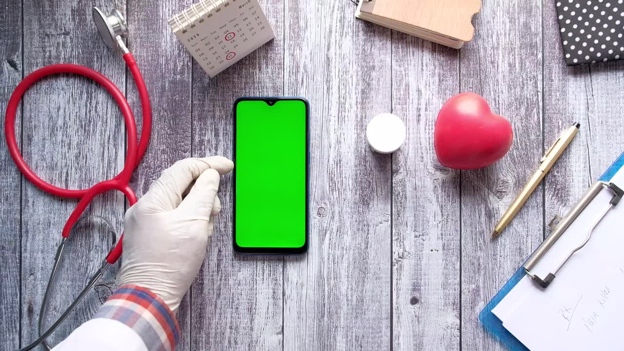 médico usando un teléfono inteligente con pantalla verde en una mesa de madera