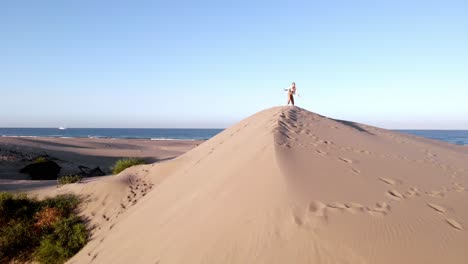 woman-dancing-on-top-of-sand,-desert-meets-sea,-aerial-shot-with-drone