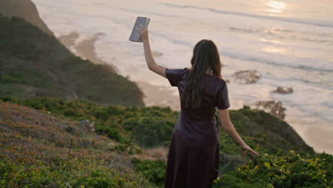 Mädchen-Geht-Von-Der-Küste-Zum-Meer-Hinunter-Und-Hält-Ein-Buch.-Rückansicht-Eines-Unbekannten-Mädchens,-Das-Einen-Hügel-Hinaufgeht