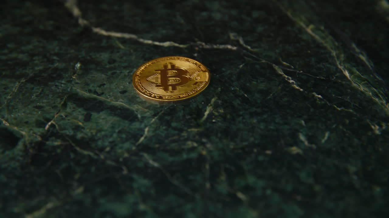 The camera slowly moves in toward a gold bitcoin lying on a richly textured dark green marble surface—highlighting the contrast between digital currency and timeless natural stone