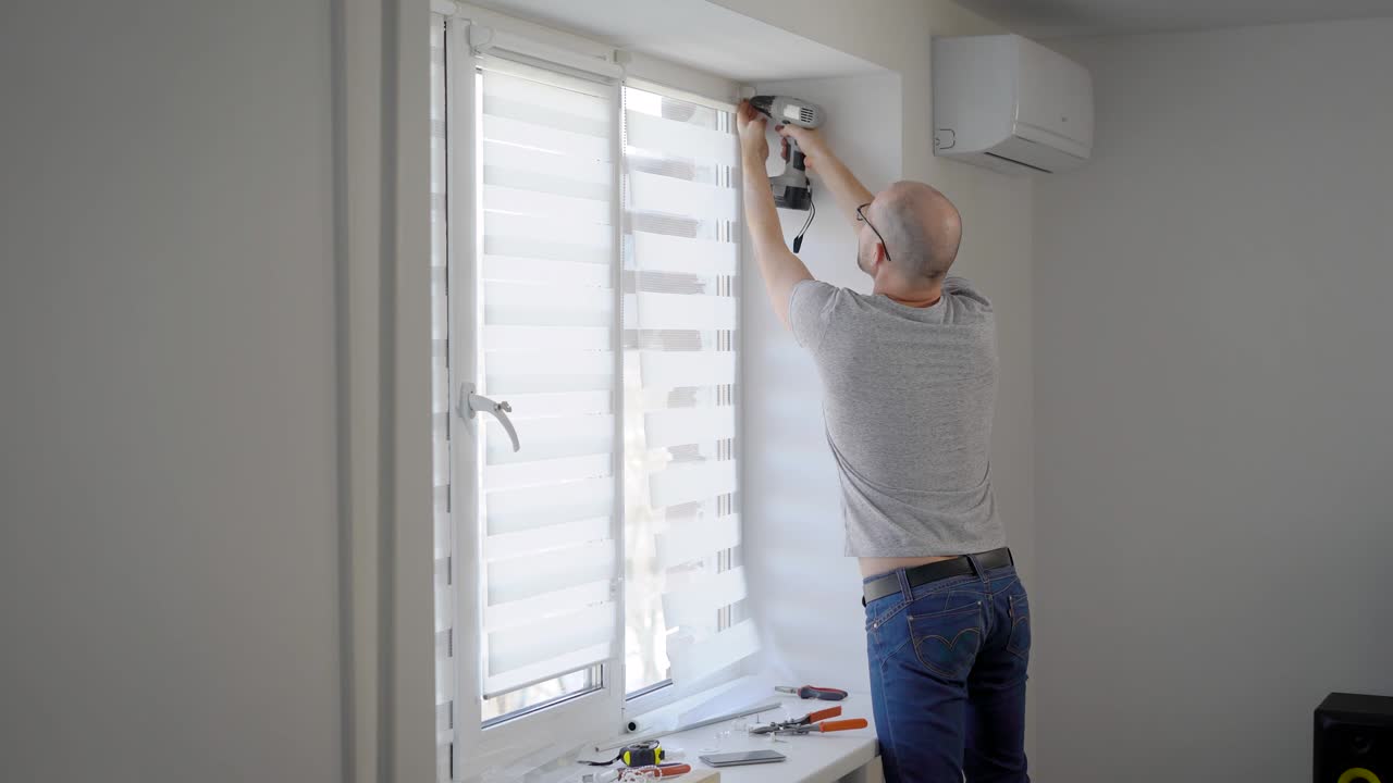 master of window installing is using electro screwdriver for rotating screw in a frame in white light room in home