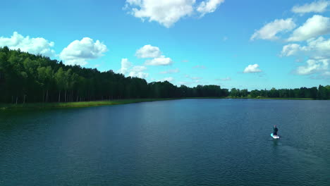 a single man is peacefully boating, absorbing truly memorable moments on a tranquil, deep blue lake clothed in rich green foliage under a progressive color sky that provides awe-inspiring sensations