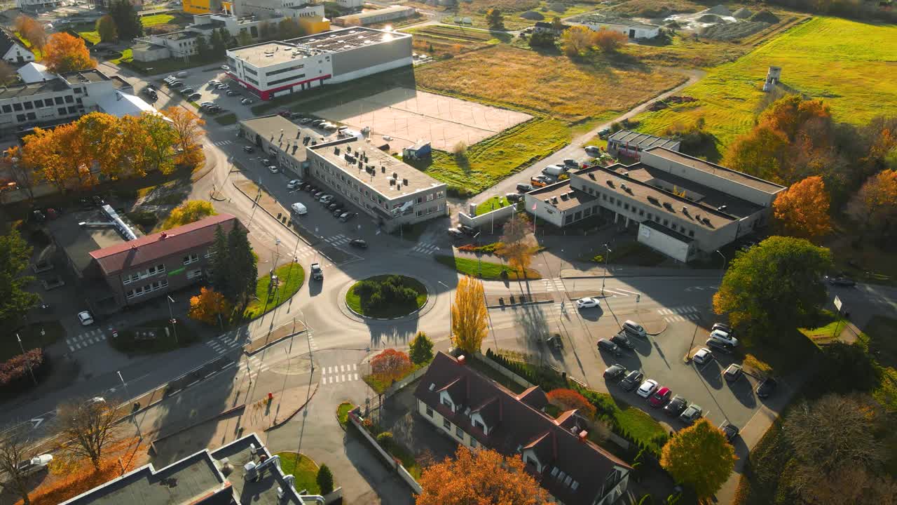 Aerial drone footage panning over a sunny autumn urban town with trees that have golden yellow autumn leaves. Cars and vehicles driving on small roads between houses and buildings in laagri Estonia