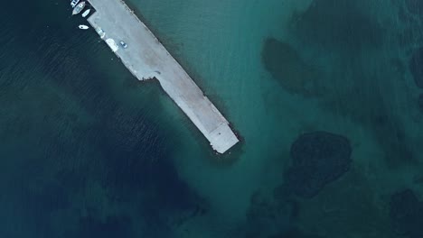 El-Dron-Disparó-Hacia-Abajo,-Capturando-Una-Escena-Costera-Con-Un-Muelle-De-Concreto,-Algunos-Barcos-Y-Agua-De-Mar-Turquesa,-A-Lo-Largo-De-Una-Playa-En-Grecia.