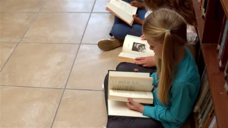 cute pupils sitting on library floor reading books