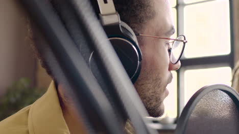 close up view of young wearing headphones sitting at a table with microphones while recording a podcast