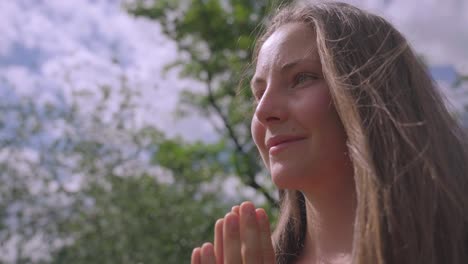 close up of white woman, smiling with hands folded in namaste pose, isolated on blurred outdoor background