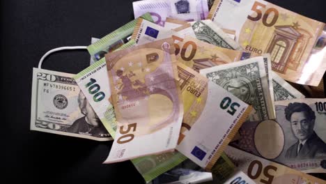 vallend geld amerikaanse dollar, europese euro, japanse yen van bovenaf op beschermend medisch masker tegen zwarte achtergrond