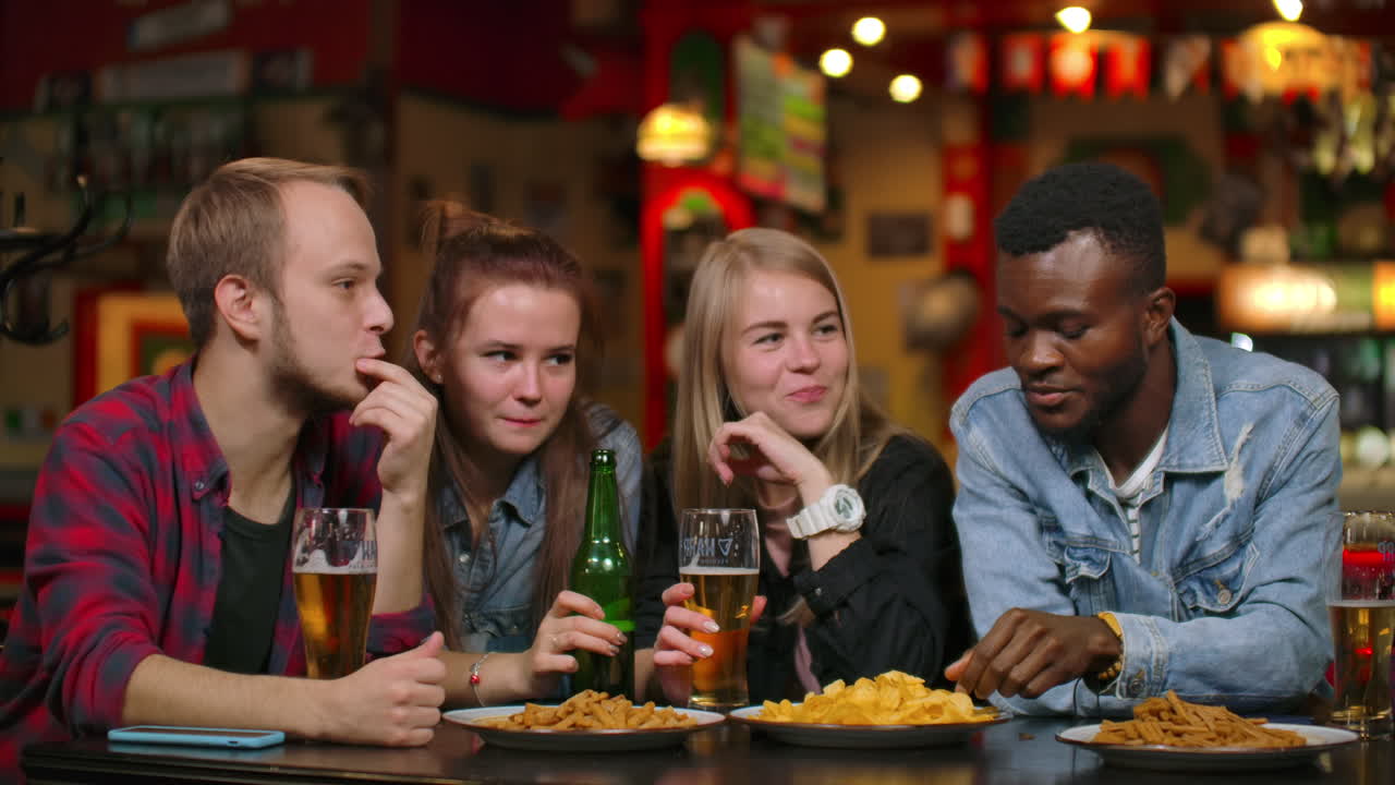 Un gruppo multietnico di 7 amici, uomini e donne, che ridono, bevono birra e fanno brindisi.