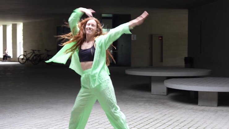 Woman dancing energetically in green outfit on urban street exuding confidence and creativity