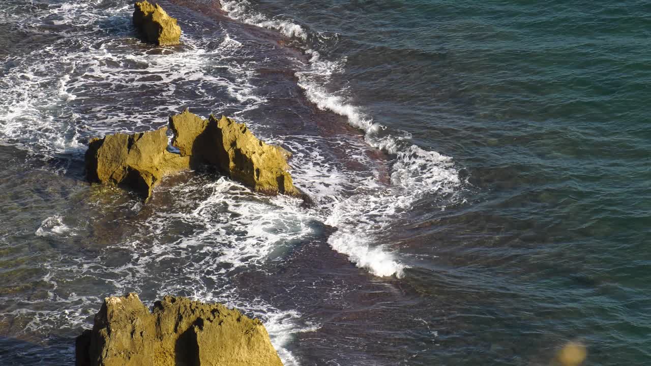 Onde dell'oceano che si infrangono su una barriera corallina rocciosa, ripresa dall'alto.