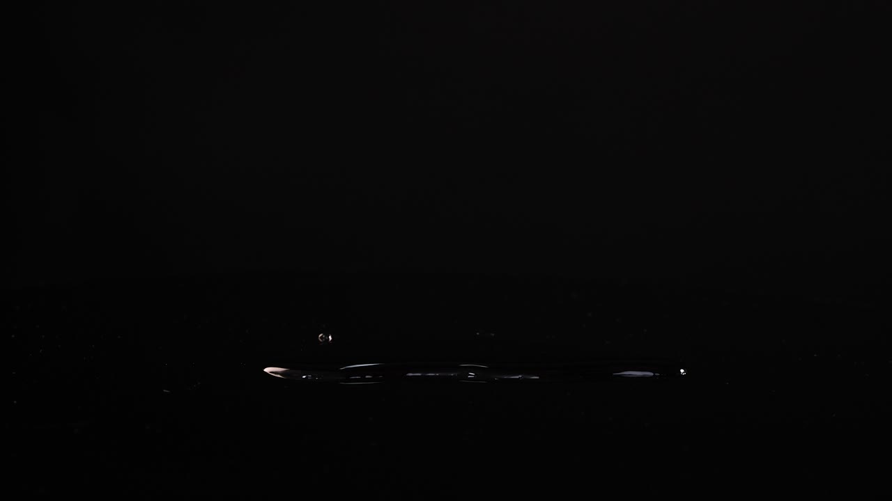 Carrots fall onto a reflective black surface, creating a dynamic water splash effect under bright lighting