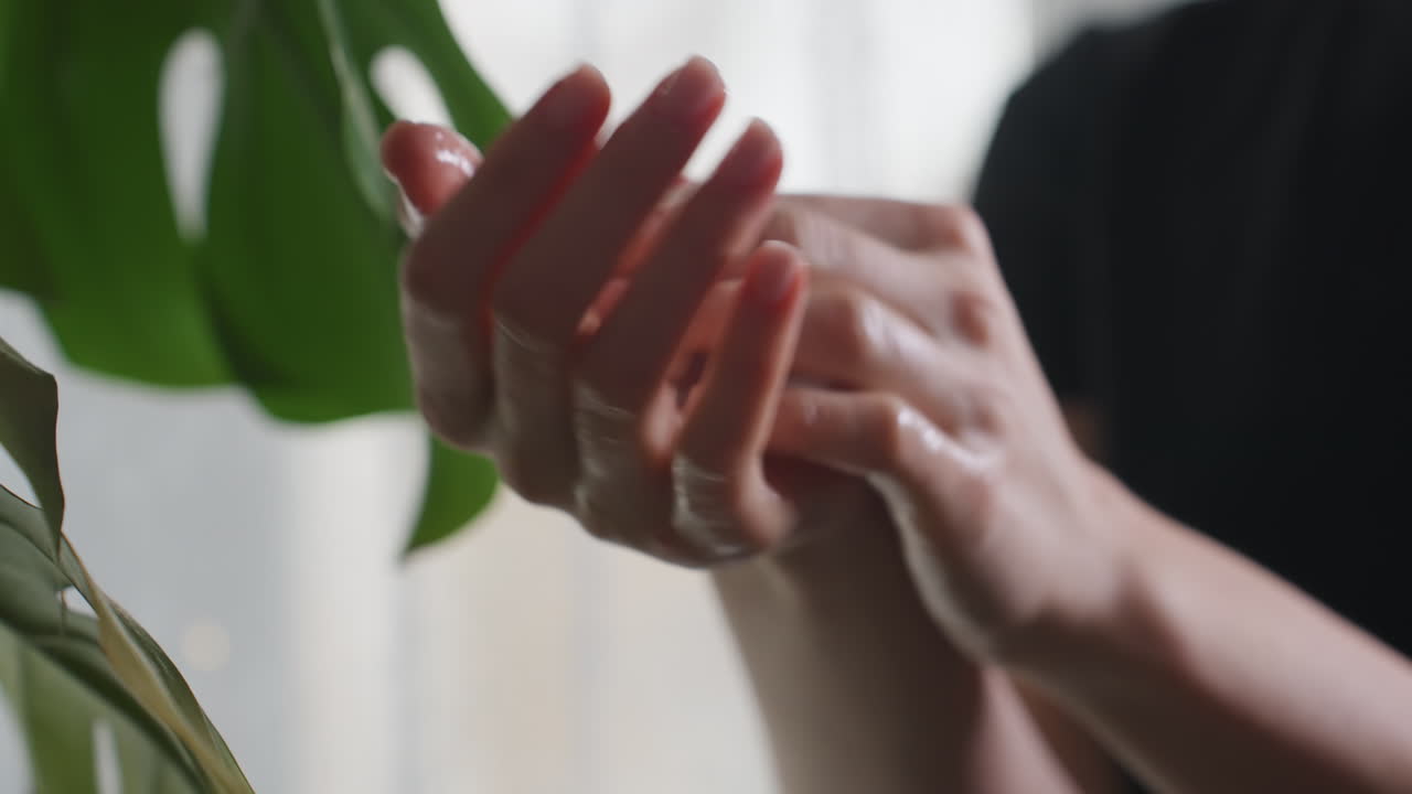 Massage therapist delicately rubbing cream into palm with moisturized fingers, close to green leaf in soft natural light, emphasizing skincare, wellness, and calm therapeutic preparation