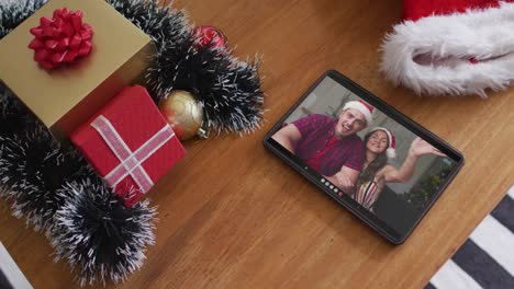 pareja caucásica sonriente con sombreros de santa en una videollamada de navidad en una tableta