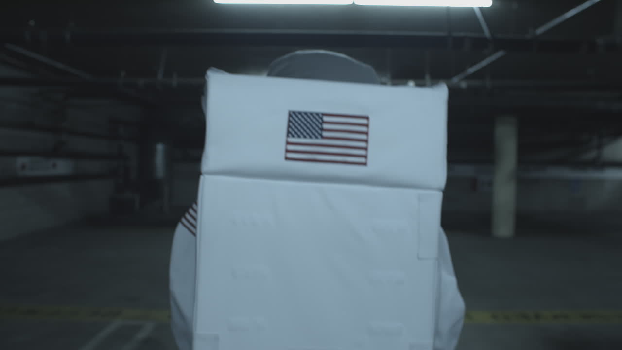 Uomo in tuta da astronauta cammina in un parcheggio sotterraneo.