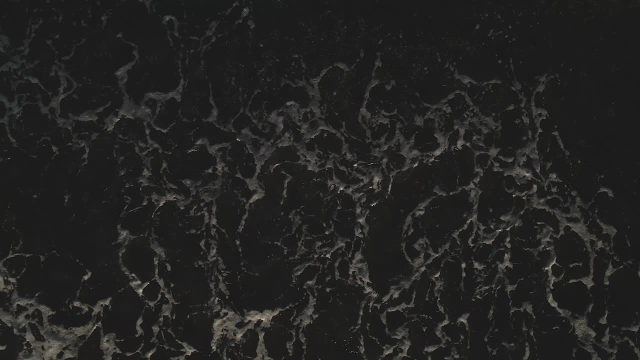 vista de ángulo alto de las olas del océano en una playa de arena oscura en 60fps