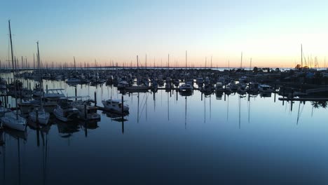 a rising high view of an early morning sunrise over a calm boat harbor full of recreational boats and vehicles