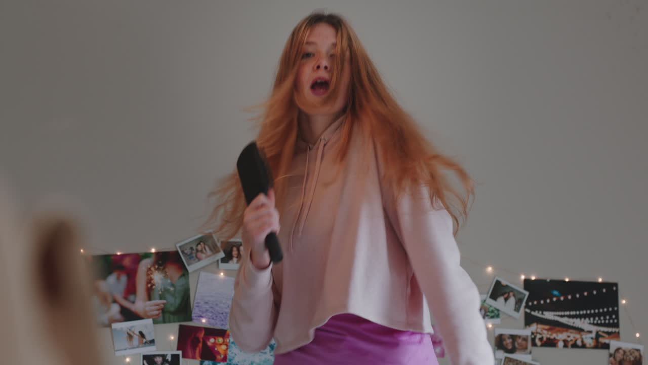 행복한 십대 소녀가 집에서 침대에 춤을 추고 음악을 즐기고 주말을 축하하고 재미있게 잠옷을 입고 침실에서 노래하고 있습니다.