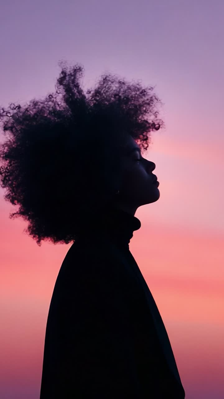 A Beautiful Silhouette of a Young Woman with Curly Hair Against a Stunning Gradient Sunset Sky in Soft Shades of Pink and Purple