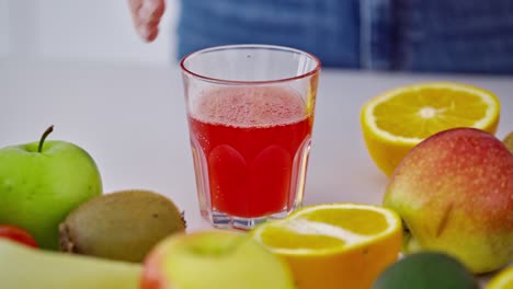 glass of fresh red juice among fruits. female's hand taking glass of freshly squeezed juice from the table. dieting concept. close-up.
