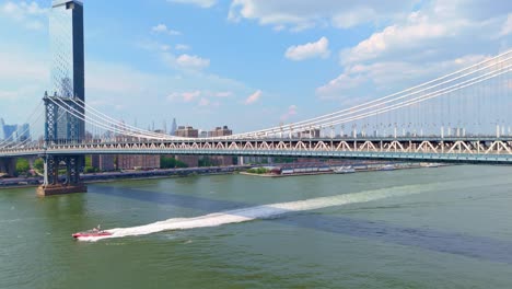 aerial view of red boat cruising under manhattan bridge with traffic in new york
