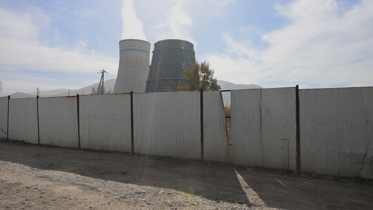Emissões de usinas termelétricas em Ulaanbaatar, Mongólia. Fumaça saindo de chaminés atrás de uma cerca branca, mostrando a infraestrutura de energia e as questões de poluição do ar.