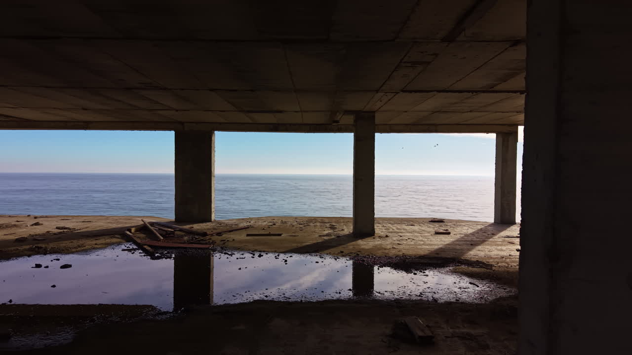 Solljuset dansar på lugnt vatten genom övergivna ruiner vid havet i gryningen
