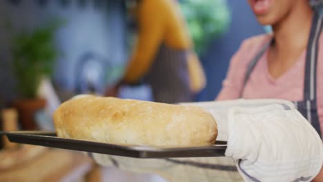 video de una pareja feliz y diversa horneando, una mujer sacando el pan del horno en la cocina, con espacio para copiar