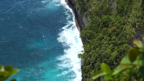 A-slow-motion-wave-crashing-at-the-bottom-of-a-cliff-at-kelingking-beach,-Nusa-Penida,-Indonesia