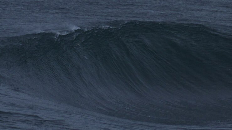 Ocean wave rises with textured water spraying mist off top as it breaks