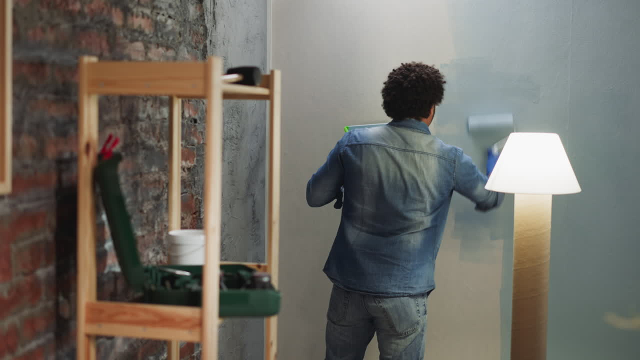 Un uomo afroamericano in camicia e jeans di denim dipinge una parete in una stanza.