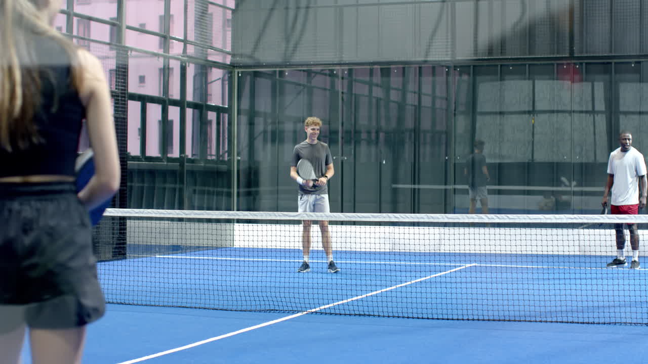 Young diverse adults playing padel tennis on blue on indoor court, focusing on intense match