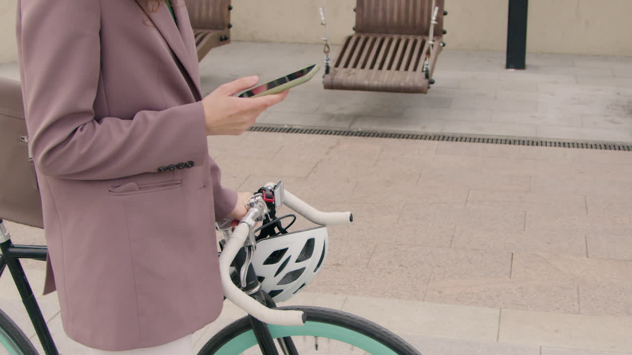 cerca de una mujer irreconocible con ropa formal caminando con una bicicleta y usando un teléfono móvil en la ciudad